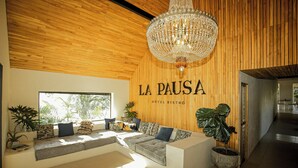 A modern hotel lobby with a wooden ceiling, a chandelier, a seating area with cushions, and a large window. - La Pausa Hotelbistro (El Peñol)