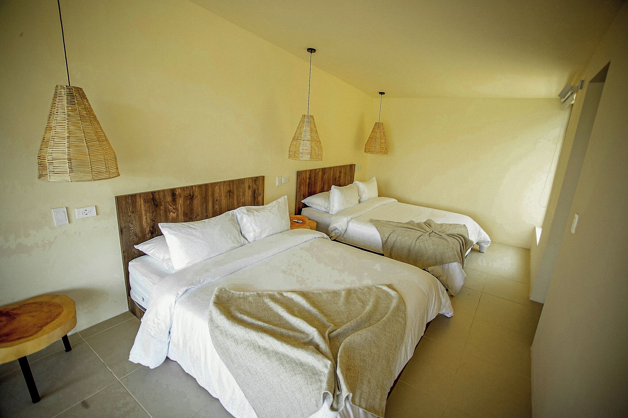 Ein Hotelzimmer mit zwei Betten, einem Holz-Kopfteil und gewebten Pendelleuchten.