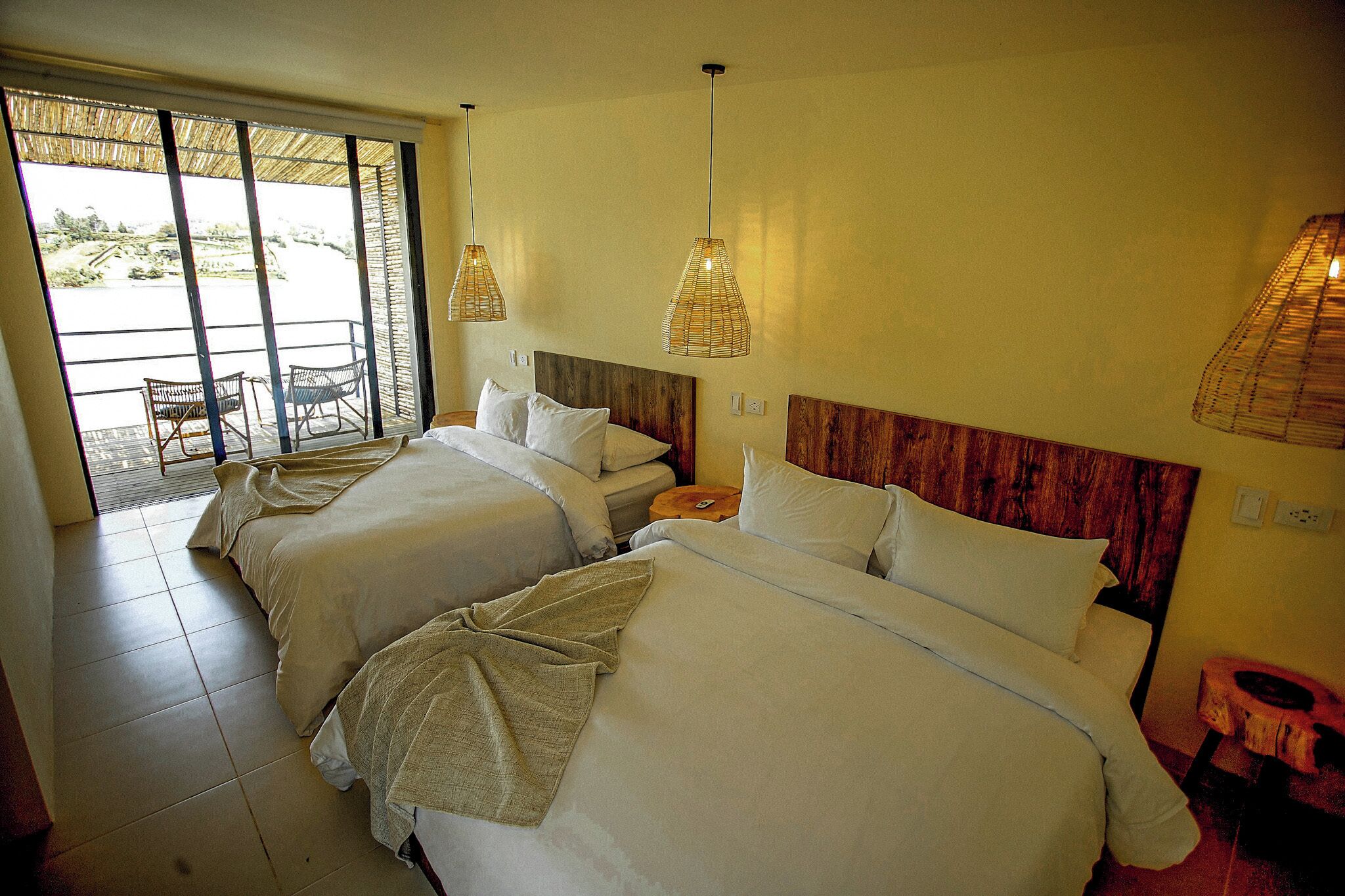 A hotel room with two beds, a balcony with chairs, and a wooden headboard.
