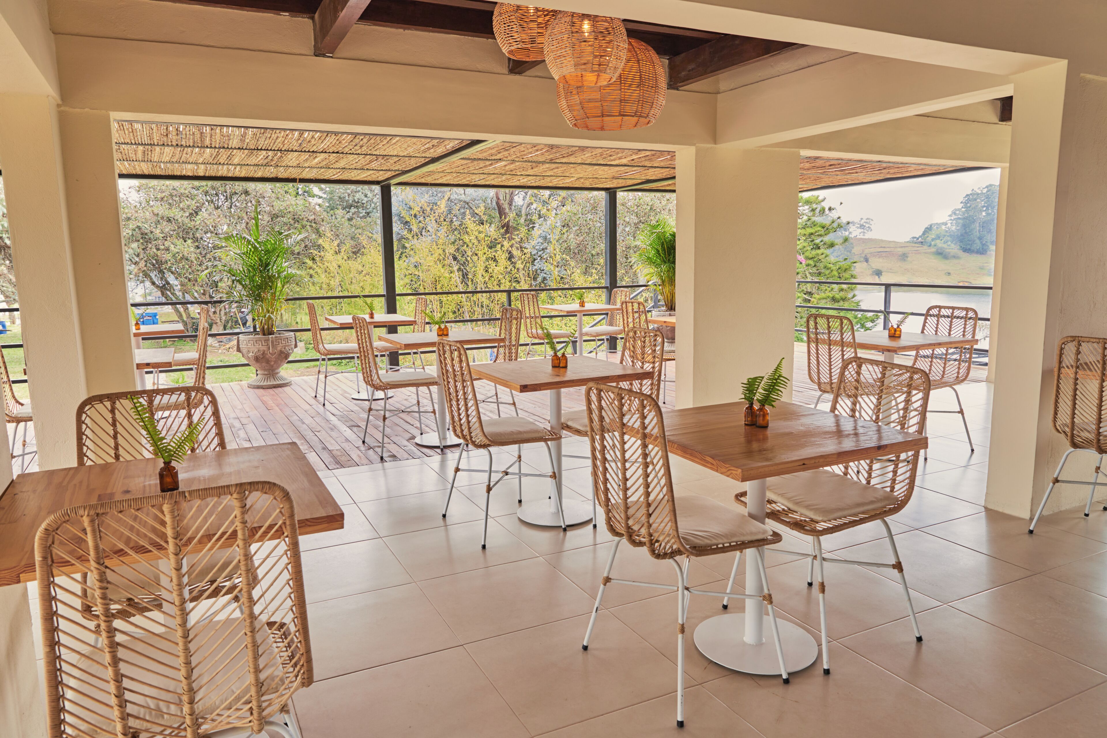 A spacious outdoor dining area with wicker chairs and tables, large windows offering views of trees and hills.