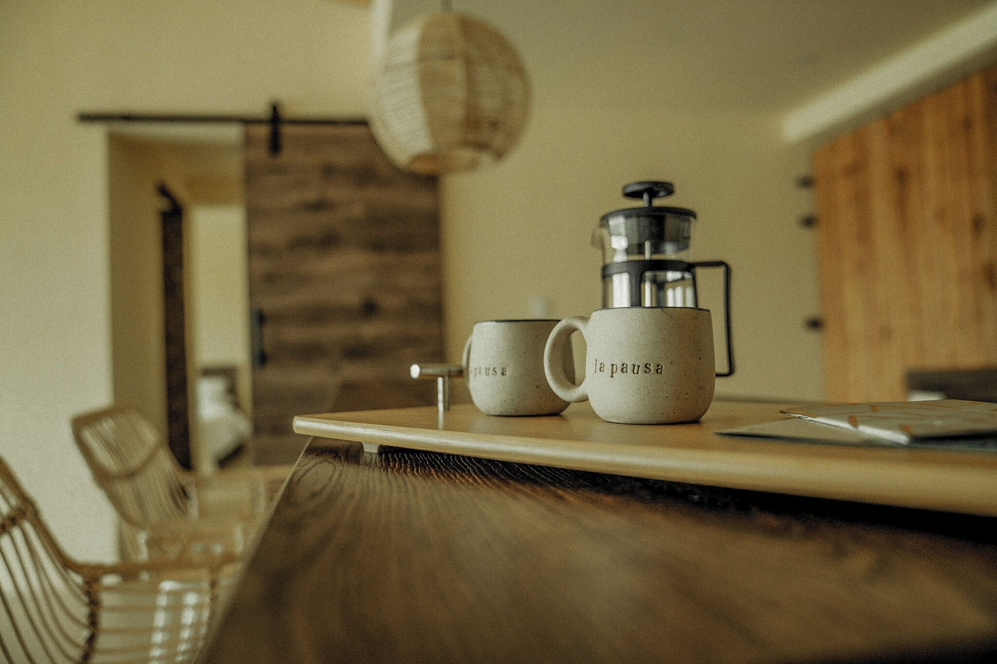 A coffee setup with a grinder and two cups labeled "la pause" on a wooden table in a room with a rustic decor.