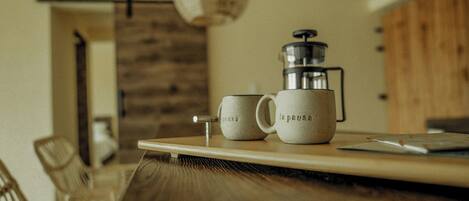 A coffee setup with a grinder and two cups labeled "la pause" on a wooden table in a room with a rustic decor.
