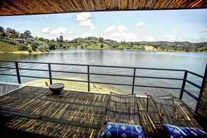 A deck with a view of a lake, a hot tub, and a seating area with cushions.