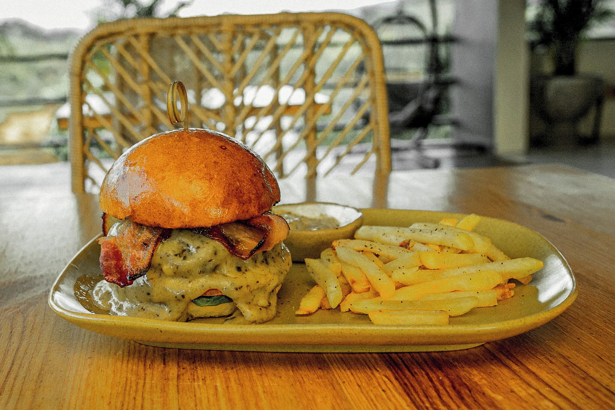 A plate with a burger, bacon, and gravy, and a side of fries on a wooden table.