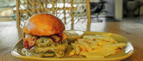 A plate with a burger, bacon, and gravy, and a side of fries on a wooden table.
