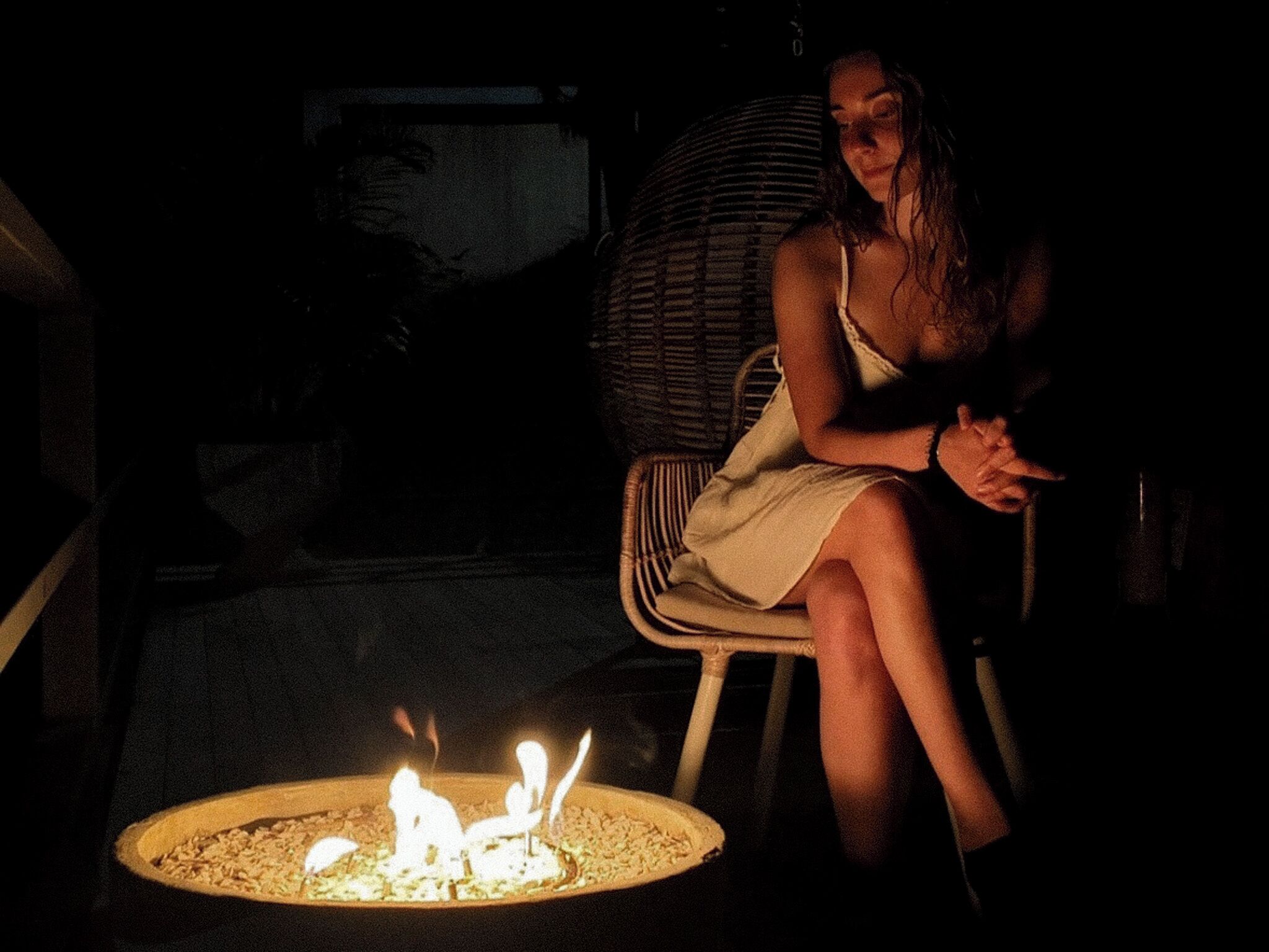 A person sitting by a fire pit in a dimly lit outdoor area.