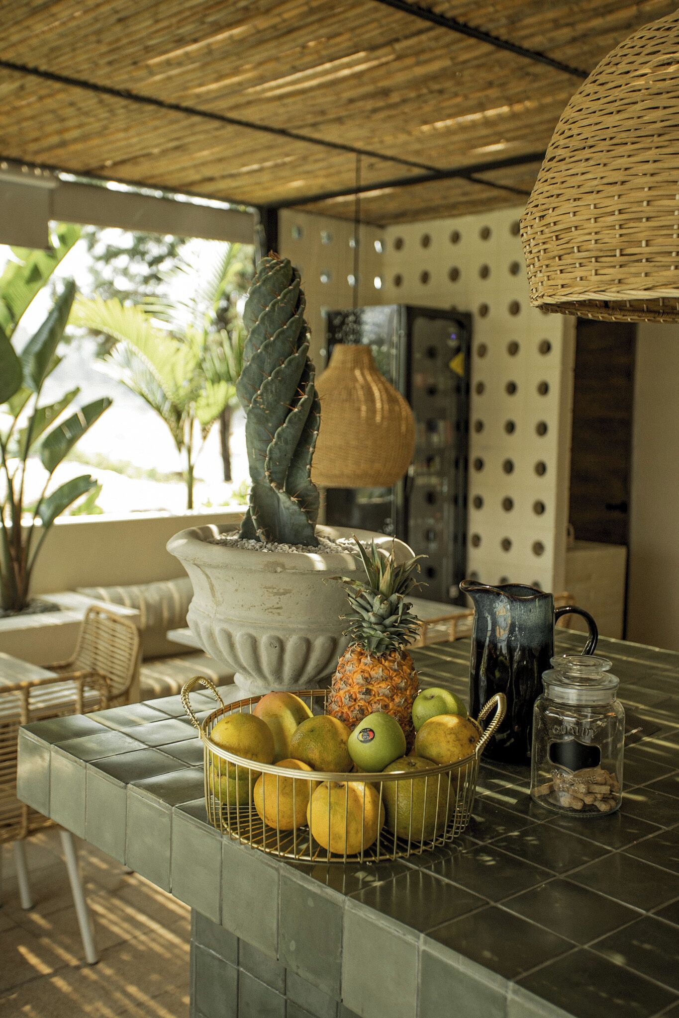 A table with a fruit basket, a potted cactus, and a hanging light fixture.