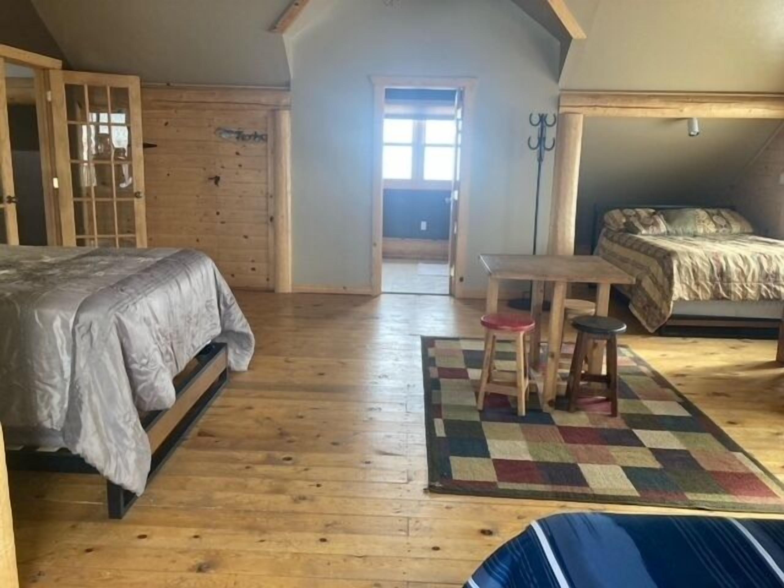 A bedroom with a bed, a small table with two stools, a window, and a door.