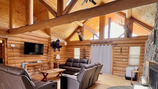 A log cabin interior with a fireplace, leather recliners, a flat-screen TV, and a stone accent wall.
