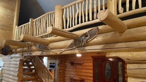A log cabin interior with a wooden staircase, a wooden door with glass panels, and a small table.