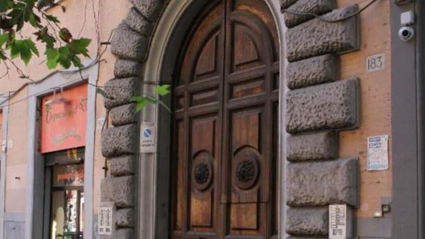 Une entrée en arc de pierre surmontée d’une porte en bois, une rue pavée et un bâtiment avec une enseigne au-dessus de la porte.