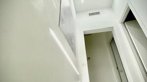 Un intérieur moderne avec un plafond en pente, une bouche d’aération visible et une porte donnant sur une autre pièce.