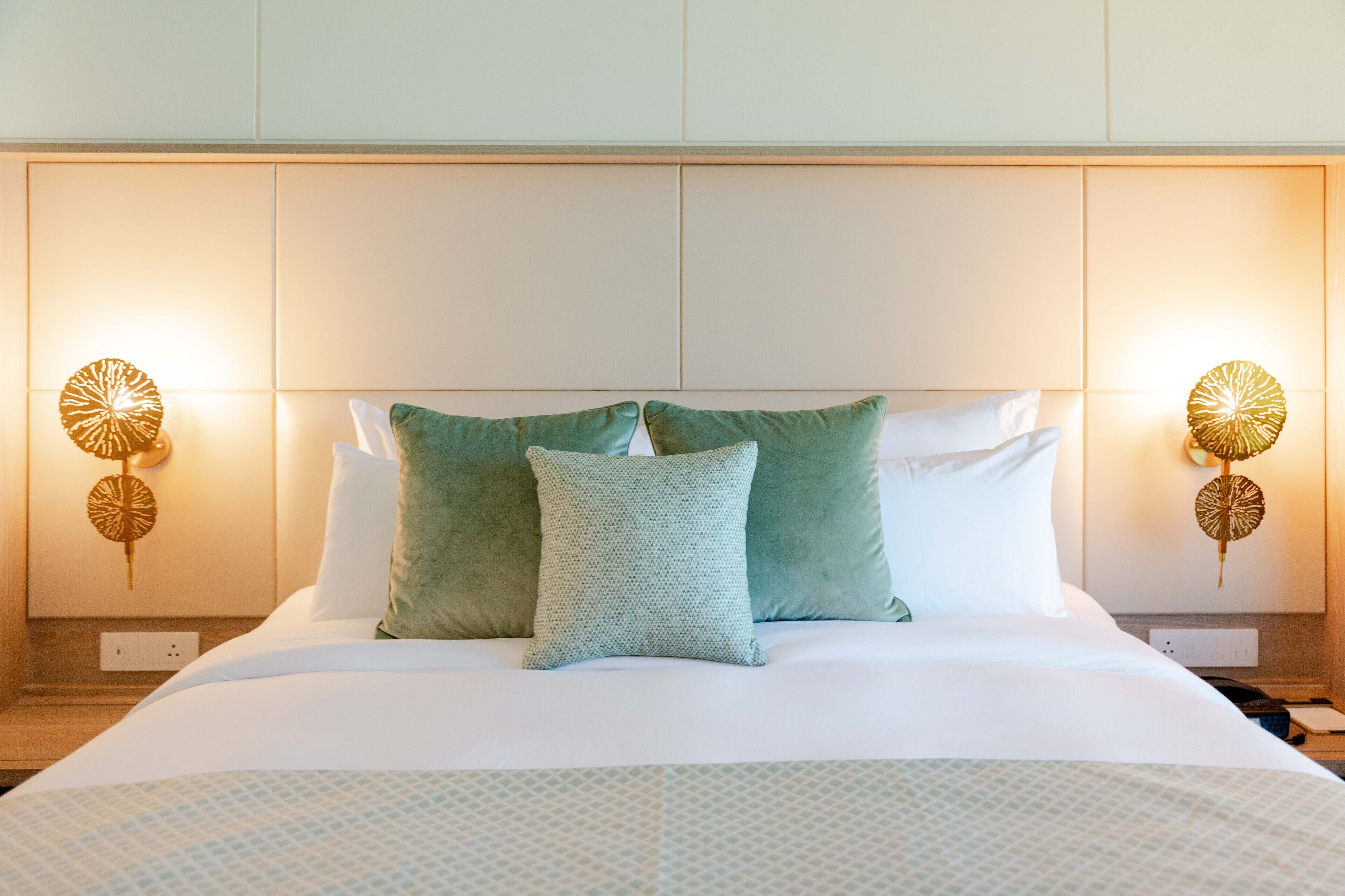Un lit bien fait, recouvert d’une couvre-lit à motifs, avec deux oreillers et deux lampes murales dotées de pieds décoratifs.