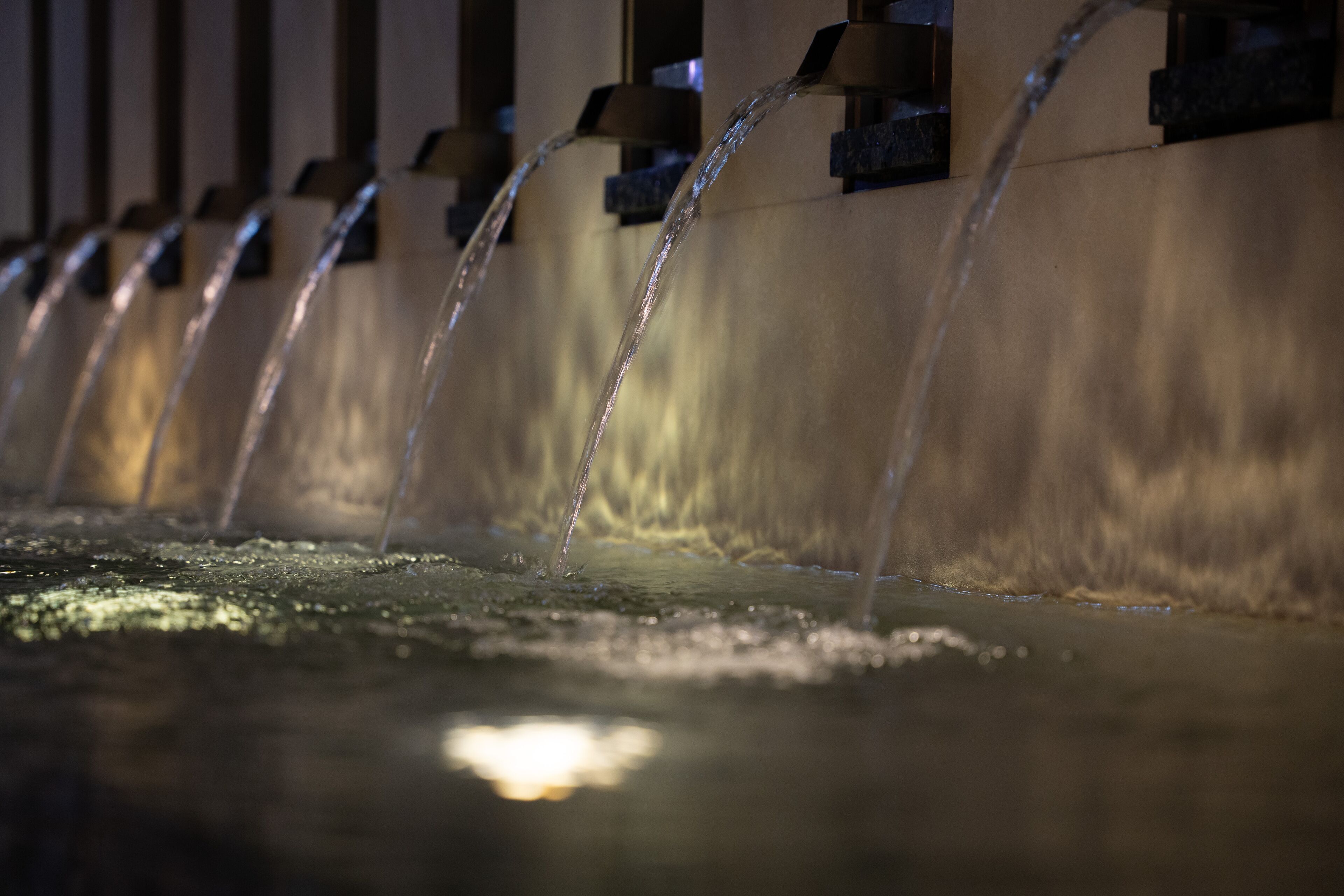 A series of water fountains with multiple streams flowing into a reflective pool.