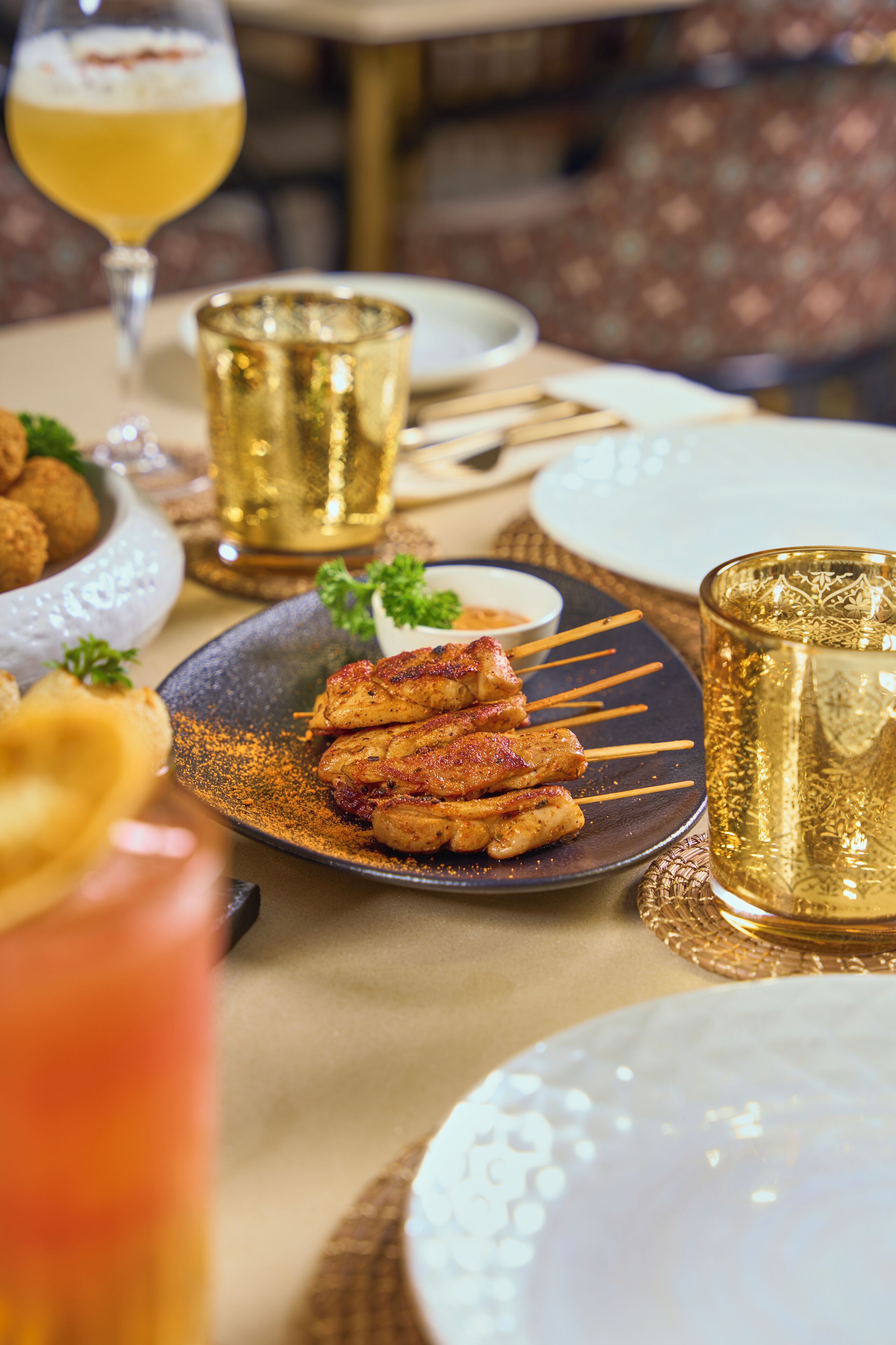Une table à manger avec des brochettes de viande grillée, un bol de sauce pour tremper et un verre de bière.