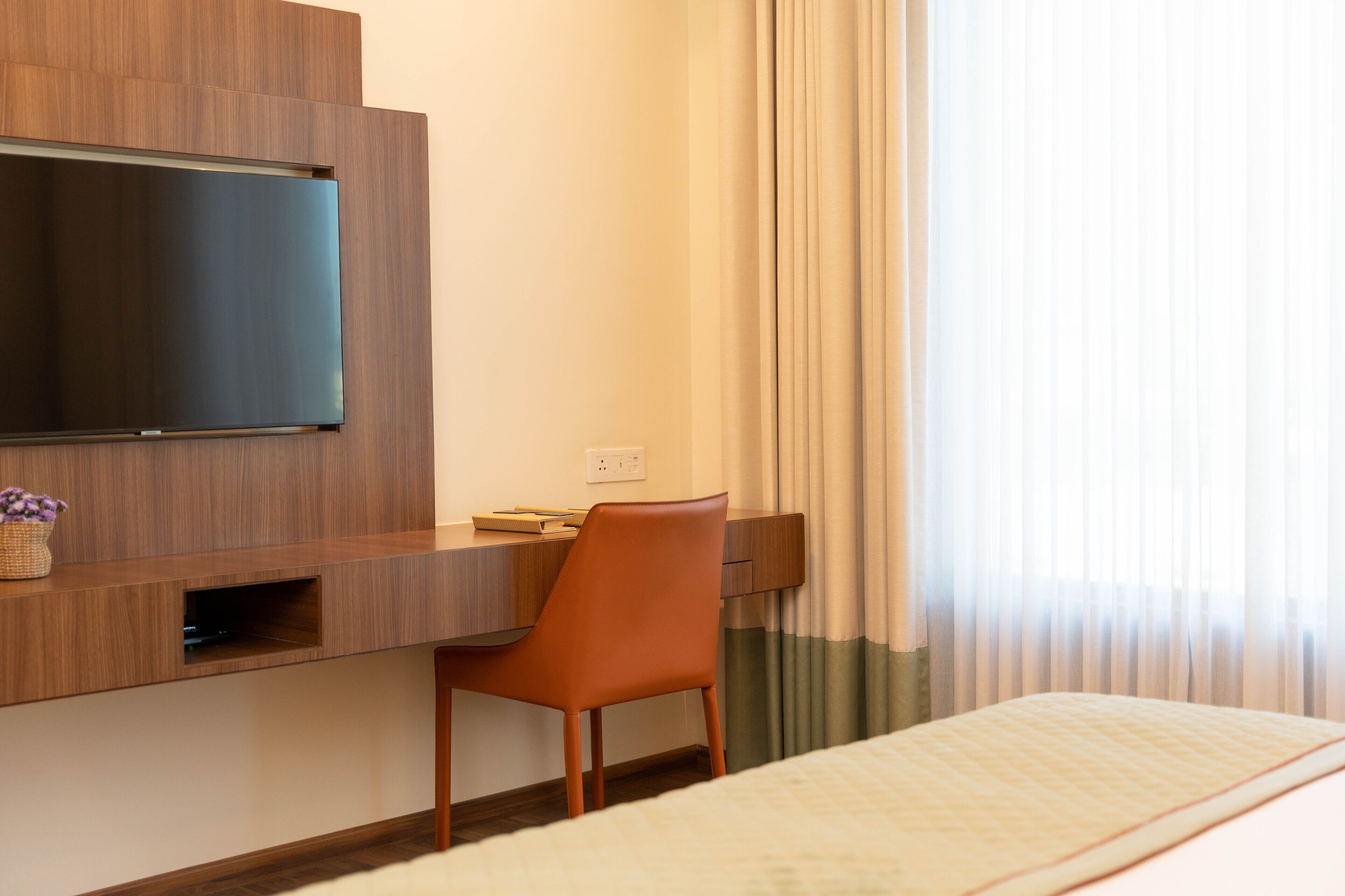 Une chambre d’hôtel comprenant un lit, un bureau avec une chaise, un téléviseur fixé au mur et une fenêtre avec des rideaux.