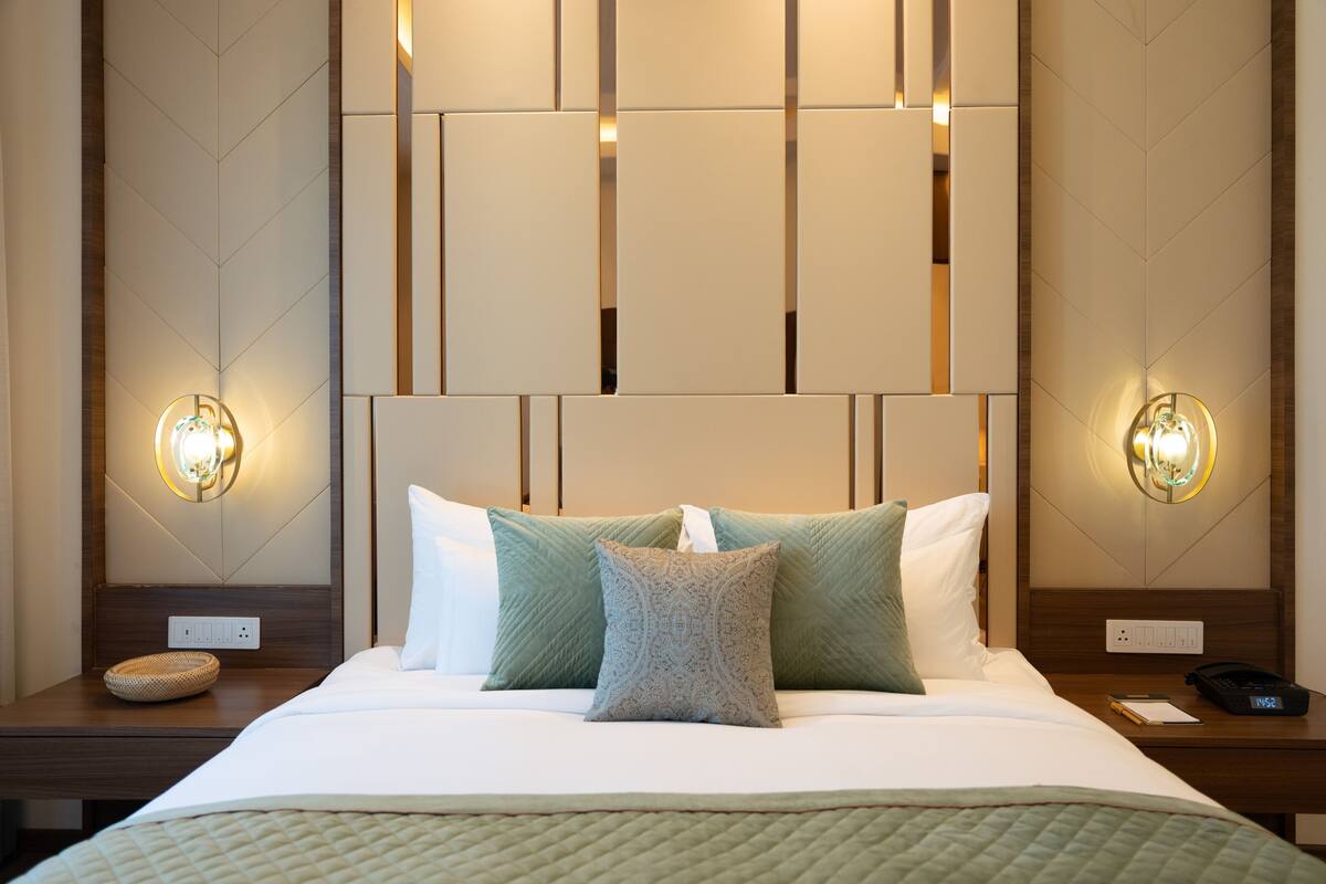 Una cama bien hecha con un edredón verde acolchado y dos almohadas, un cabecero de madera y dos lámparas de noche.