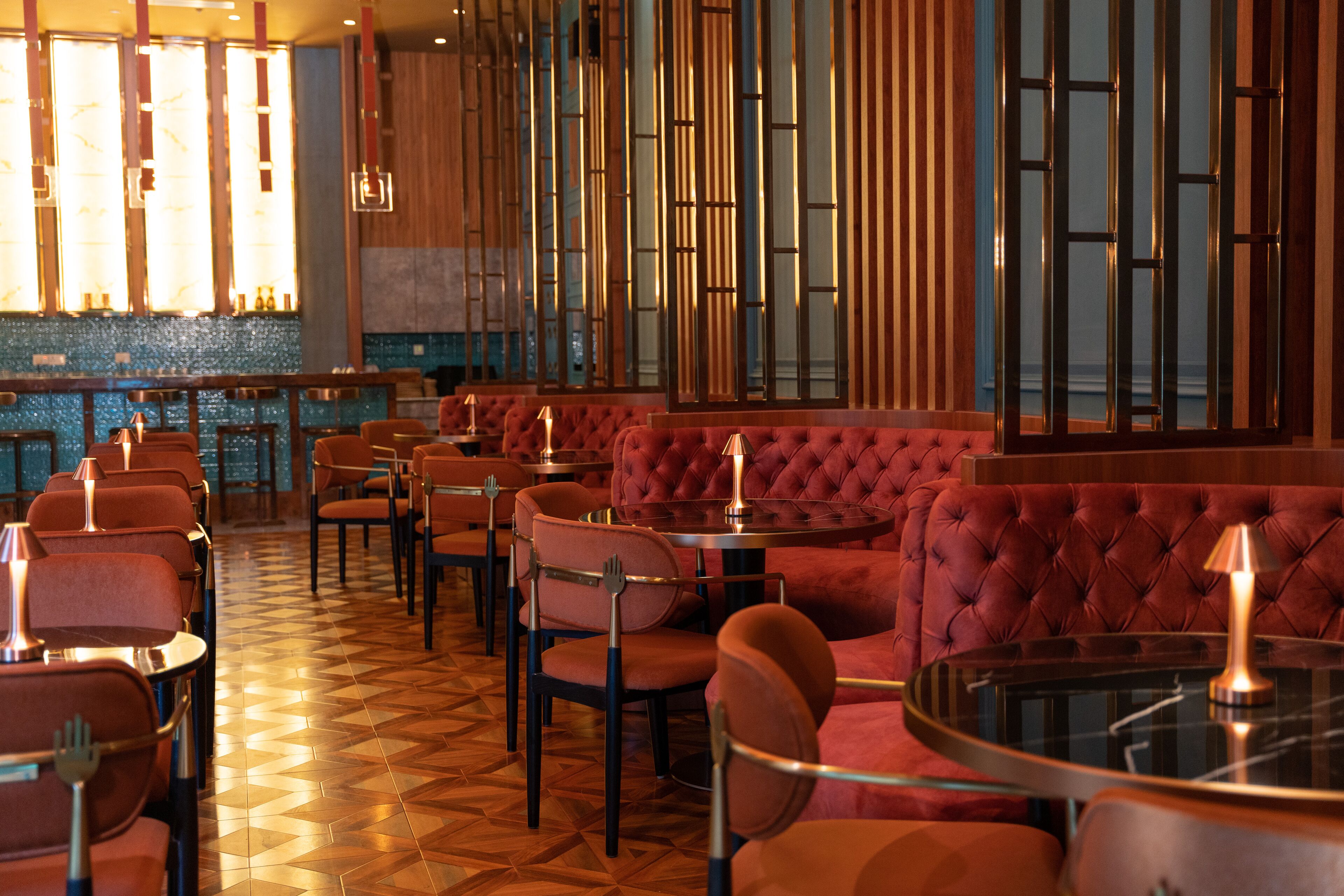 A restaurant interior with red upholstered booths, round tables, and a patterned floor.