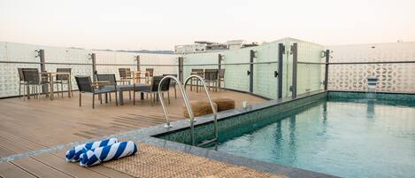 Un área de piscina en la azotea con sillones de descanso, una escalera de piscina y una piscina pequeña.