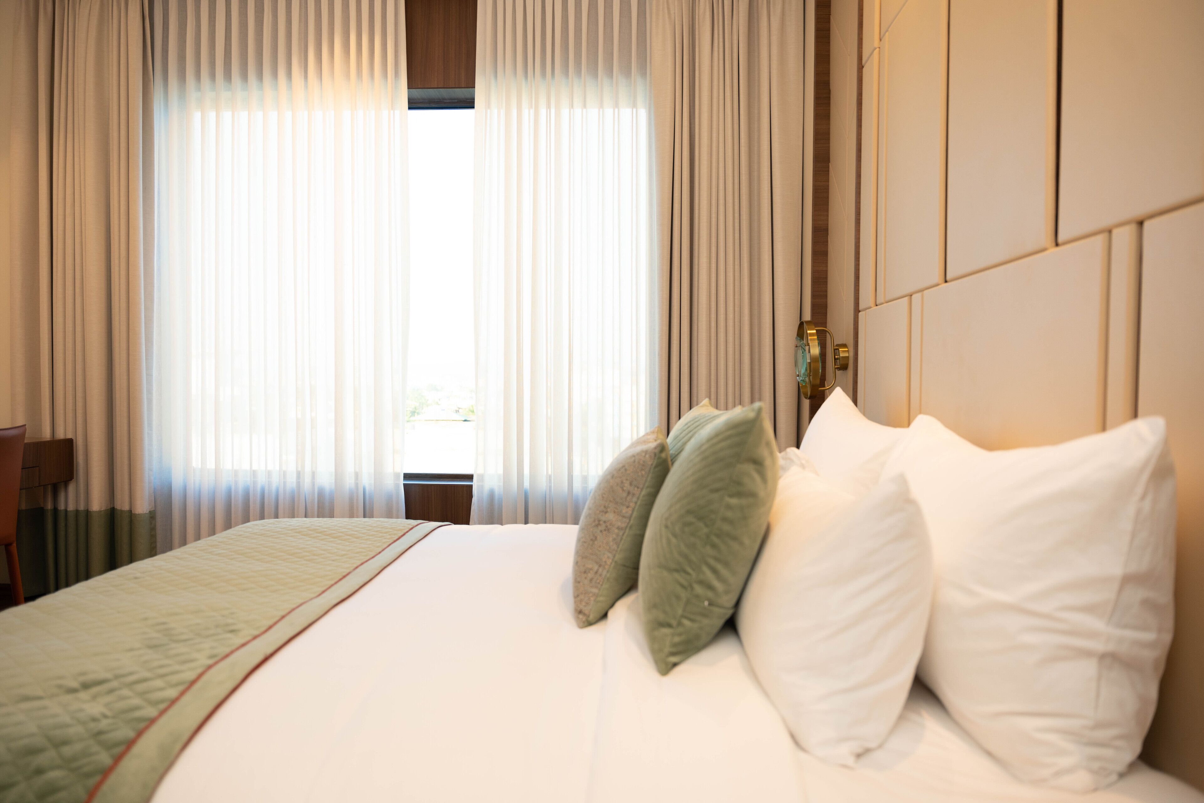 Habitación de hotel con una cama grande, cortinas color beige y un cabecero con reloj incorporado.