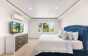 Quarto moderno com uma cama grande, televisão, penteadeira e janela com vista para o verde.