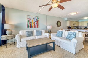 A living room with a ceiling fan, a coffee table, and a painting on the wall. - C602 | Beachfront with Beach Service, Pool, & WiFi (Miramar Beach)