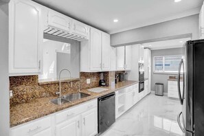 Une cuisine moderne avec des meubles blancs, des plans de travail en granit, un évier en acier inoxydable et un lave-vaisselle noir.