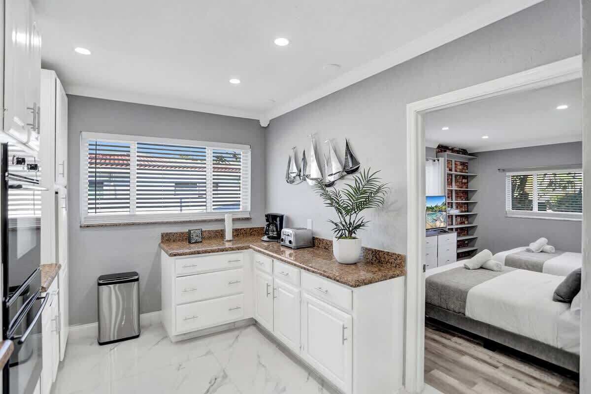 A modern kitchen with white cabinets, a granite countertop, and a stainless steel trash can.