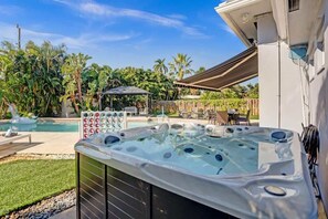 Un bain à remous avec une piscine en arrière-plan, entouré de palmiers et d’un belvédère.