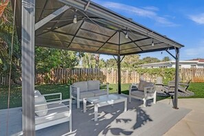 Une terrasse extérieure dotée d’un espace salon couvert, comprenant un canapé, des fauteuils et une table.