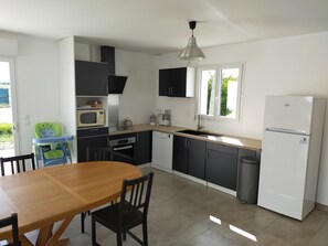 Une cuisine compacte avec une table en bois, des placards noirs, un réfrigérateur blanc et une fenêtre laissant entrer la lumière naturelle.