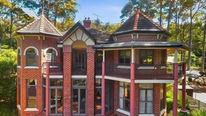 A two-story brick house with a balcony, a tower-like structure, and a covered porch. - The Castle Lilli Pilli Beach (LILLI PILLI)