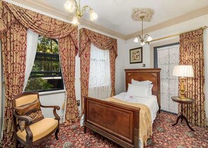 A bedroom with a wooden bed, a chair, a lamp, and patterned curtains. - The Castle Lilli Pilli Beach (LILLI PILLI)