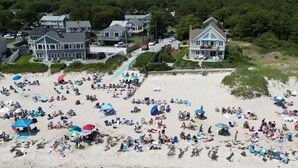 A beach with numerous umbrellas and people, surrounded by houses and a forested area. - 🌊 BEACHFRONT FAMILY HOME - 2026 Vrbo Rental Of The Year Award! (Yarmouth)