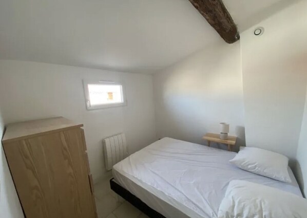 A small, white room with a single bed, a wooden wardrobe, a small table with a lamp, and a window providing natural light. - Charming apartment in an old building, center of Montpellier (Montpellier)