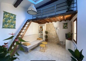 A loft-style bedroom with a sloped ceiling, a bed, a ladder, and a stone wall. - Charming apartment in an old building, center of Montpellier (Montpellier)