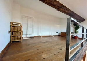 Relax in a spacious room with a high ceiling and exposed beams, featuring a large open floor, staircase, and a cozy reading nook.