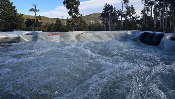 Un jacuzzi rodeado por un paisaje natural con árboles y colinas al fondo.