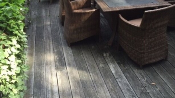 Eine Terrass mit Holzdeck, Korbmöbeln und einem großen Sonnenschirm.