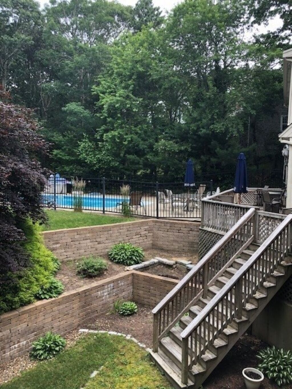 A backyard with a brick patio, a wooden staircase, a pool, and a fence.