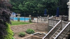 Ein Garten mit Ziegelterrasse, Holztreppe, Schwimmbecken und Zaun.