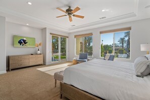 Quarto com cama grande, ventilador de teto, televisão, cômoda e vista para o exterior.