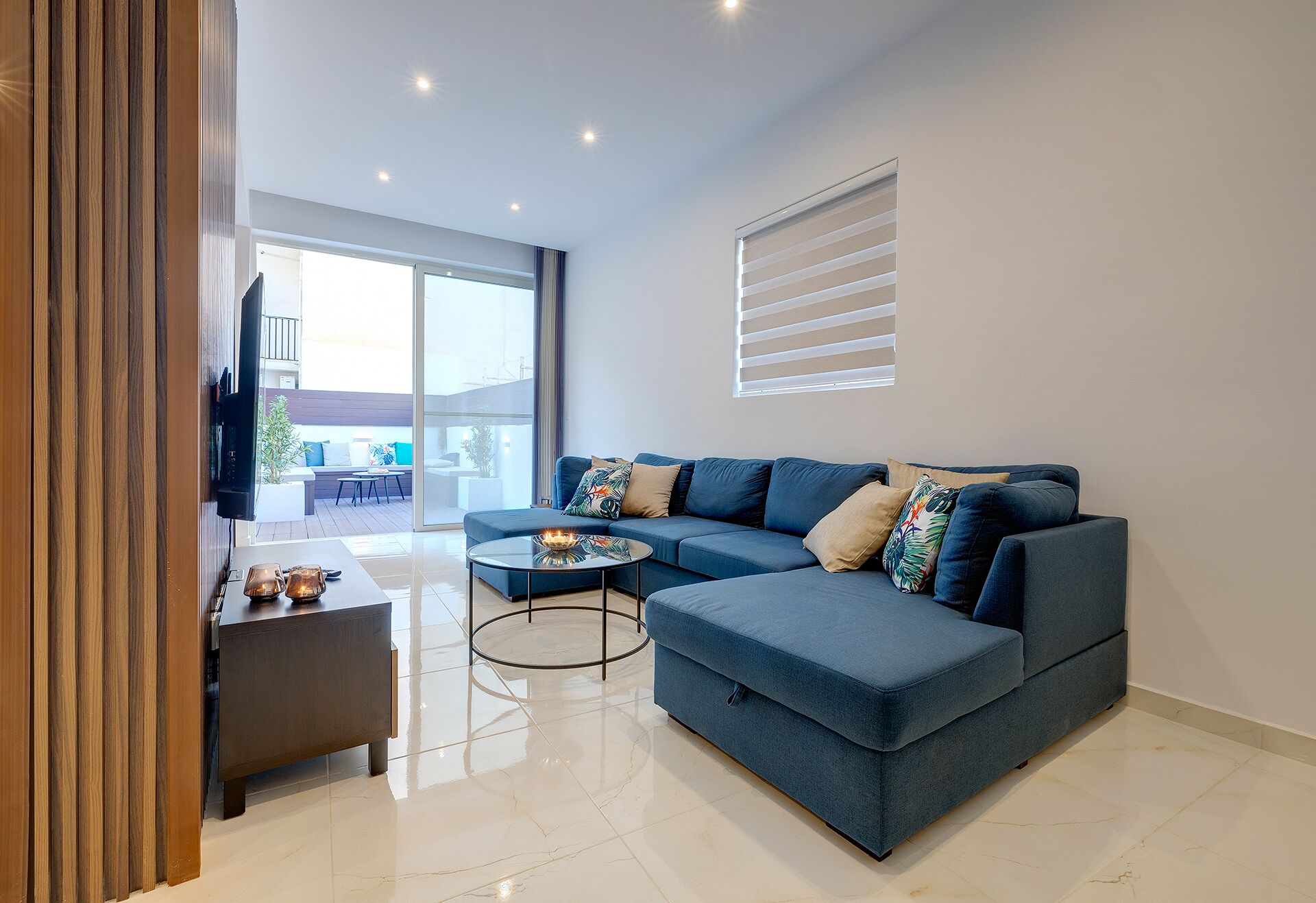 Una sala de estar moderna con un sofá seccional azul, una pequeña mesa redonda y un televisor montado en la pared.