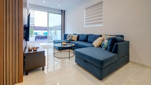 Una sala de estar moderna con un sofá seccional azul, una pequeña mesa redonda y un televisor montado en la pared.