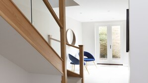 Un interno moderno con una scala in legno, una sedia blu e una porta che dà su uno spazio esterno.