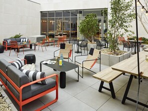 An outdoor seating area with various chairs and tables, a sofa, and a large window overlooking the interior of a building. - Tribe Paris Saint Ouen (Saint-Ouen)