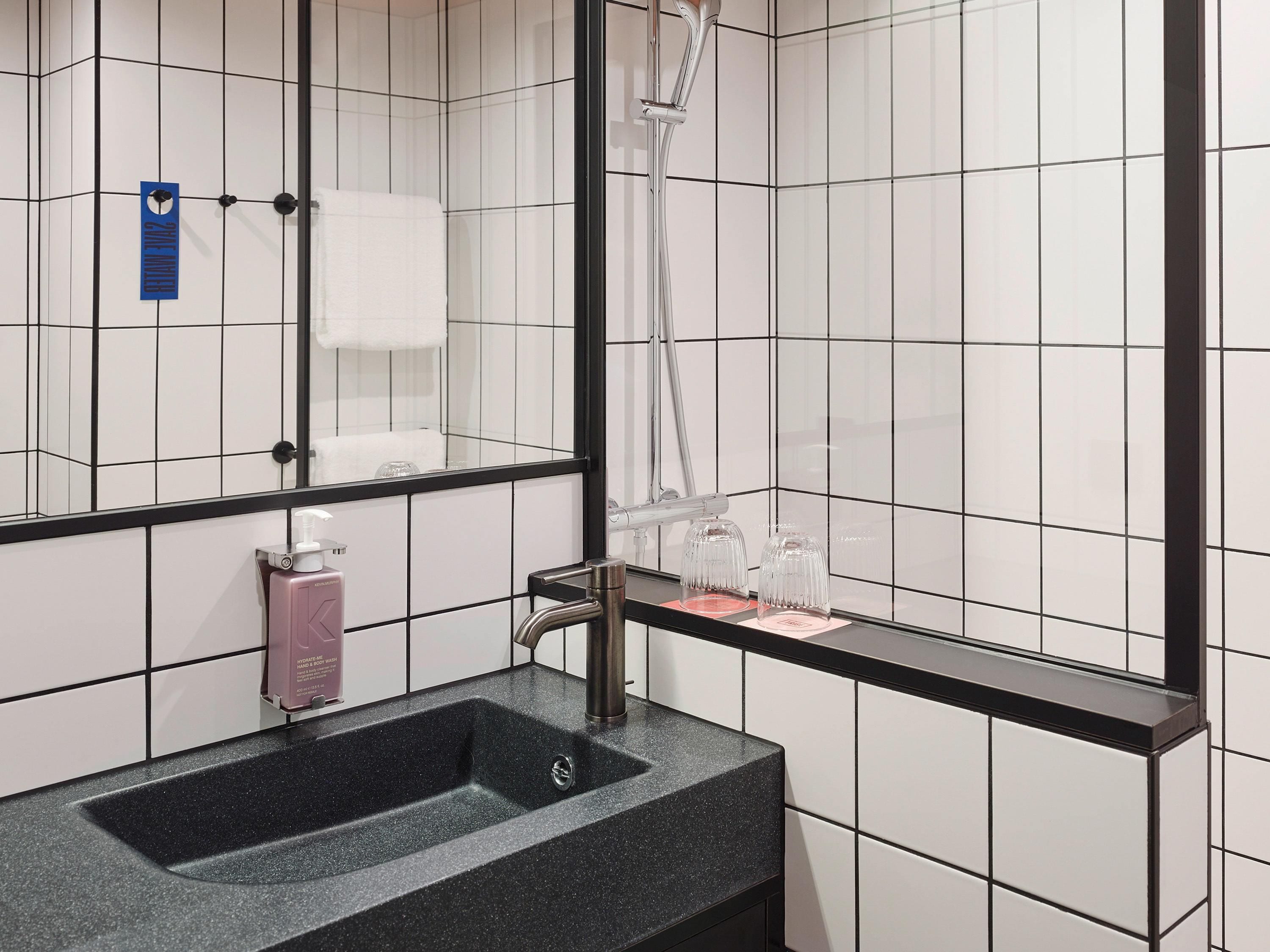 Un baño con un lavamanos negro, un espejo y un perchero para toallas.