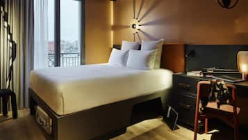 Una habitación de hotel moderna con una cama grande, un escritorio con lámpara y vistas a la ciudad a través de la ventana.