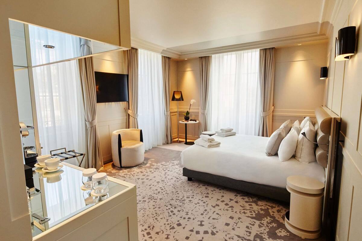 Une chambre d’hôtel avec un grand lit, une table de chevet, une chaise, un miroir et un téléviseur.