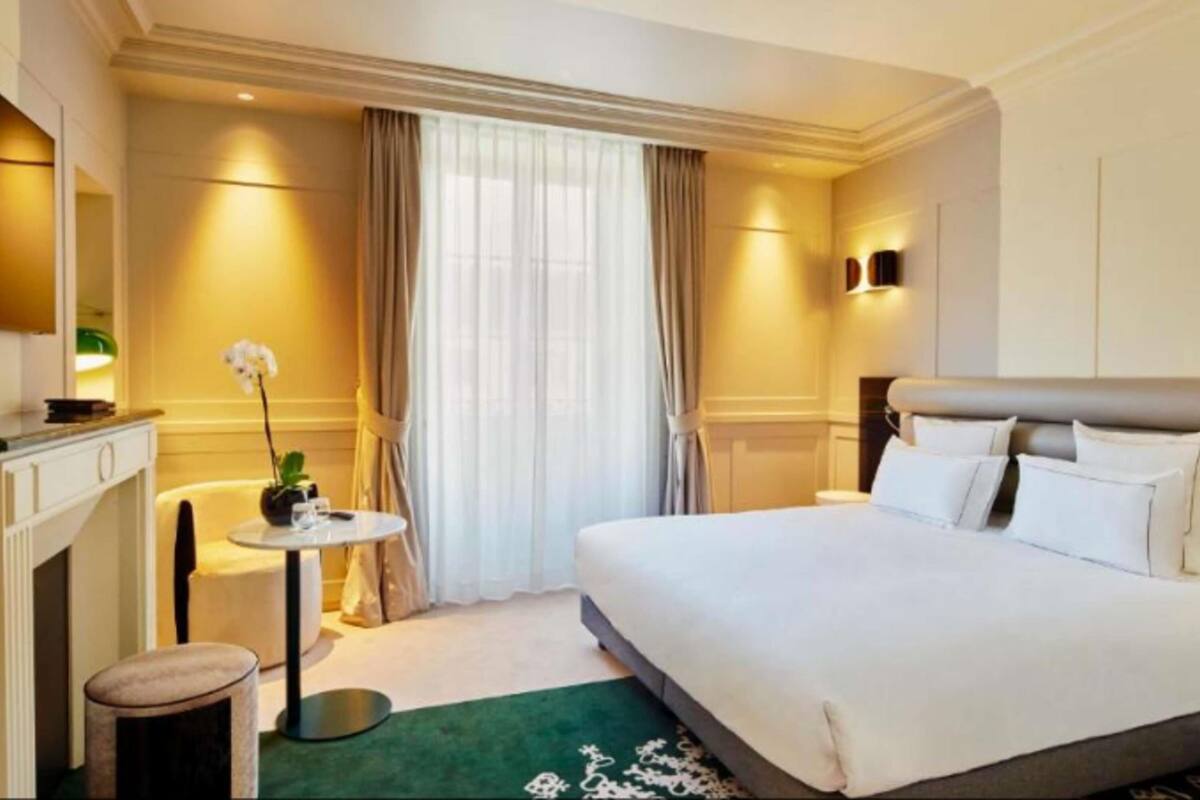 Une chambre d’hôtel avec un grand lit, un petit bureau, une chaise, une table ronde et une plante en pot.